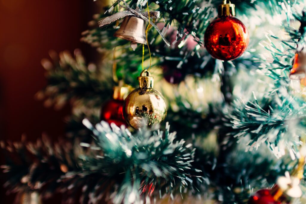 Árvore de natal vista de perto, em foco uma bola de natal dourada e outra vermelha, além de um sino.