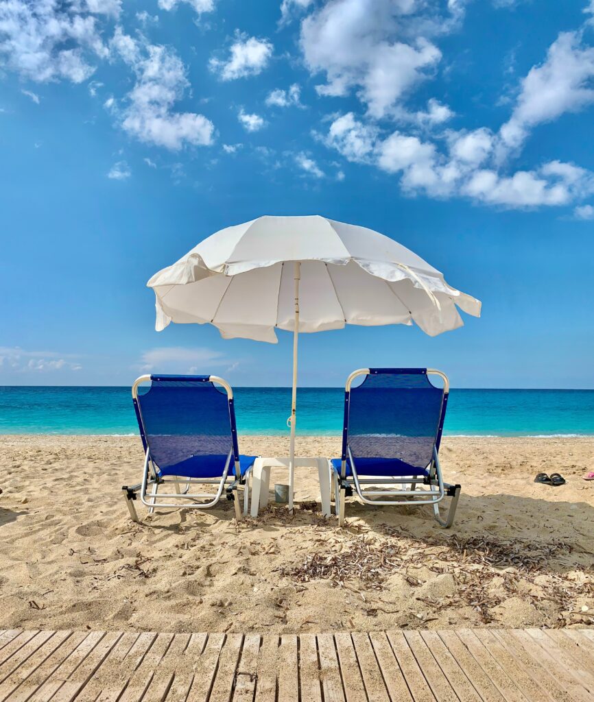 cadeiras de praia azul com guarda-sol branco na areia, em um dia ensolarado. Férias de verão.