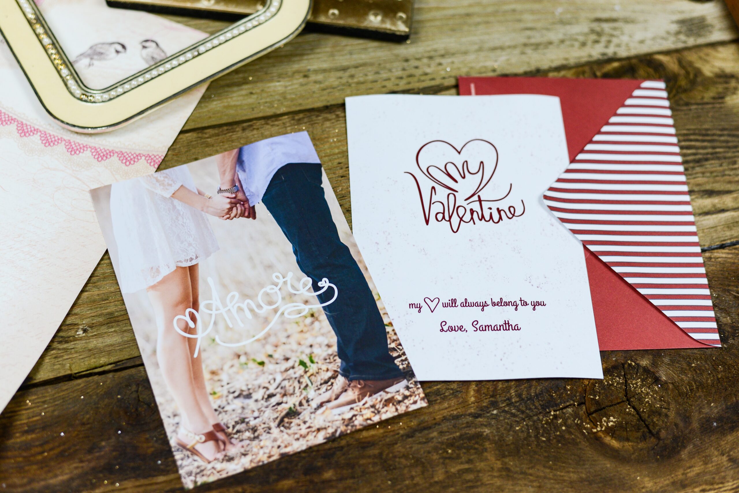 Mesa com um envelope e dois cartoês de "Valentine's Day". Um tem uma imagem de um casal, mostrando dos pés à cintura e tem escrito "Amor". O outro tem um coração desenhado estilizado com os escritos "My Valentine".